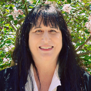 PatricePetro_Headshot Patrice Petro, the Dick Wolf Director of the Carsey-Wolf Center, appears against a background of green leaves and pink flowers. She has long black hair and is smiling.