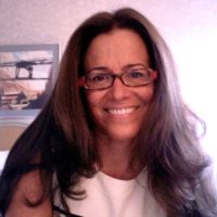 Cristina Venegas, a professor of Film and Media Studies at UC Santa Barbara, poses against a pink background. She has long brown hair and glasses, and she is smiling.