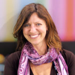 An image of Professor Jennifer Holt against a multicolored striped background. Professor holt has reddish brown shoulder length hair. She is wearing a pink scarf, and is smiling.