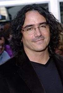 BradSilberling_Headshot Headshot of director Brad Silberling. It depicts a man with shoulder length hair in glasses, a black button up shirt, and a black blazer. He is smiling and appears to be posed in front of a crowd of people.