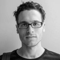 A headshot of cinematographer Isaak Liptzin. He is shot in black and white against a neutral background, and wears glasses and a dark shirt.