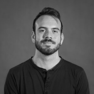 ValerioCiriaci_Heatshot Black and white portrait of filmmaker Valerio Ciriaci. The image depicts a middle aged man posed in front of a neutral background smiling for the camera.