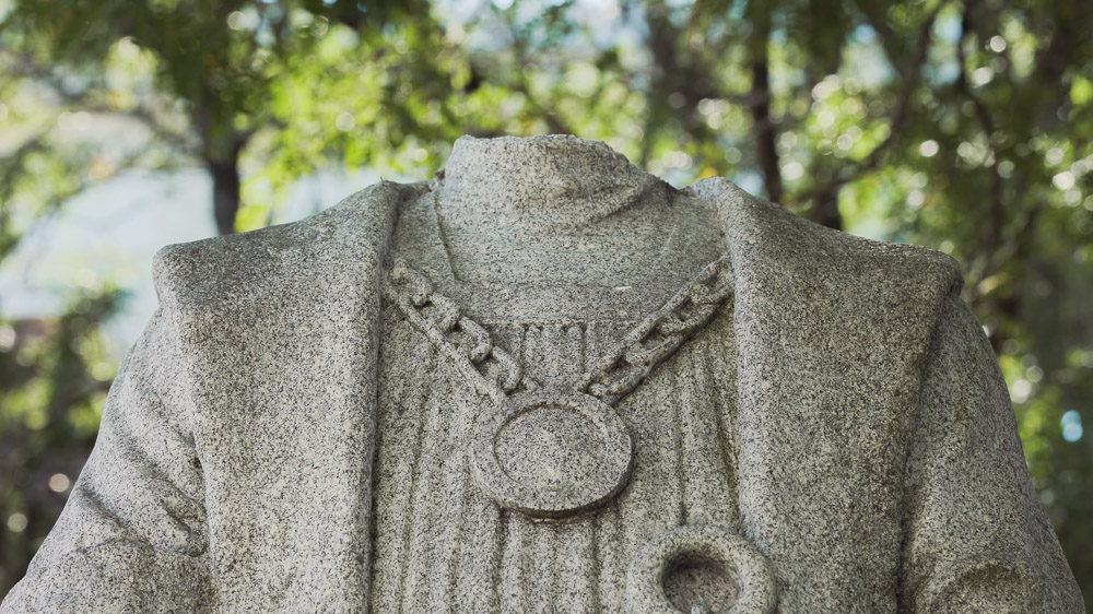 A close-up image of a stone statue of Christopher Columbus with its head removed.