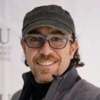 Head shot of filmmaker Sam Kadi. The image depicts a man wearing glasses and a news cap. He is smiling towards the camera.