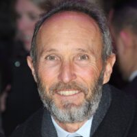 A headshot of producer Steve Starkey. He wears a dark wool coat, a grey scarf and a black necktie. He is smiling for the camera at an outdoor event.