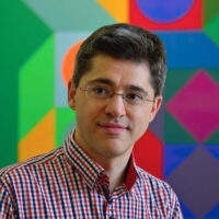 Headshot of Dr. Márton Orosz. A man with dark hair and glasses in front of a colorful geometric artwork.