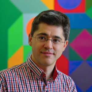 Márton_Orosz Headshot of Dr. Márton Orosz. A man with dark hair and glasses in front of a colorful geometric artwork.