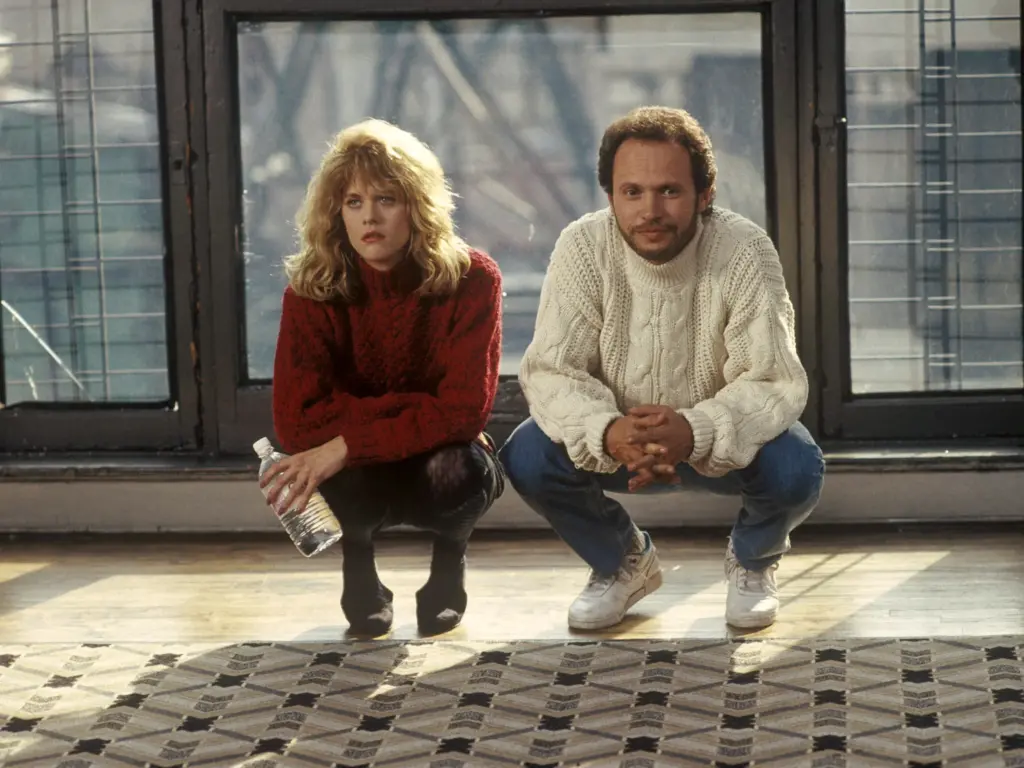 A promotional still for the film When Harry Met Sally, from the scene where they are unrolling a new carpet in Harry's apartment. The image depicts a man and a woman squatting in front of a carpet and looking pensive. The woman(sally) is blonde, she wears a knit red sweater, a skirt and tights; she holds a water bottle and appears frustrated. The man (harry) wears a white knit sweater, blue jeans, and white sneakers; he appears more playful.