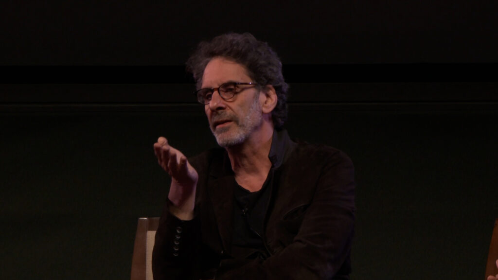 Joel Coen, director of The Tragedy of Macbeth, on stage during a Q&A at the Pollock Theater. He is wearing a black jacket and eyeglasses.