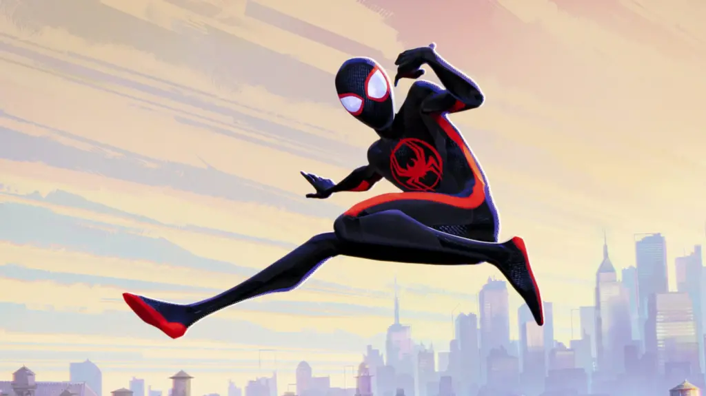 A still from Across the Spider-Verse, featuring Miles Morales in his black suit with red accents swinging against a city scape backdrop.