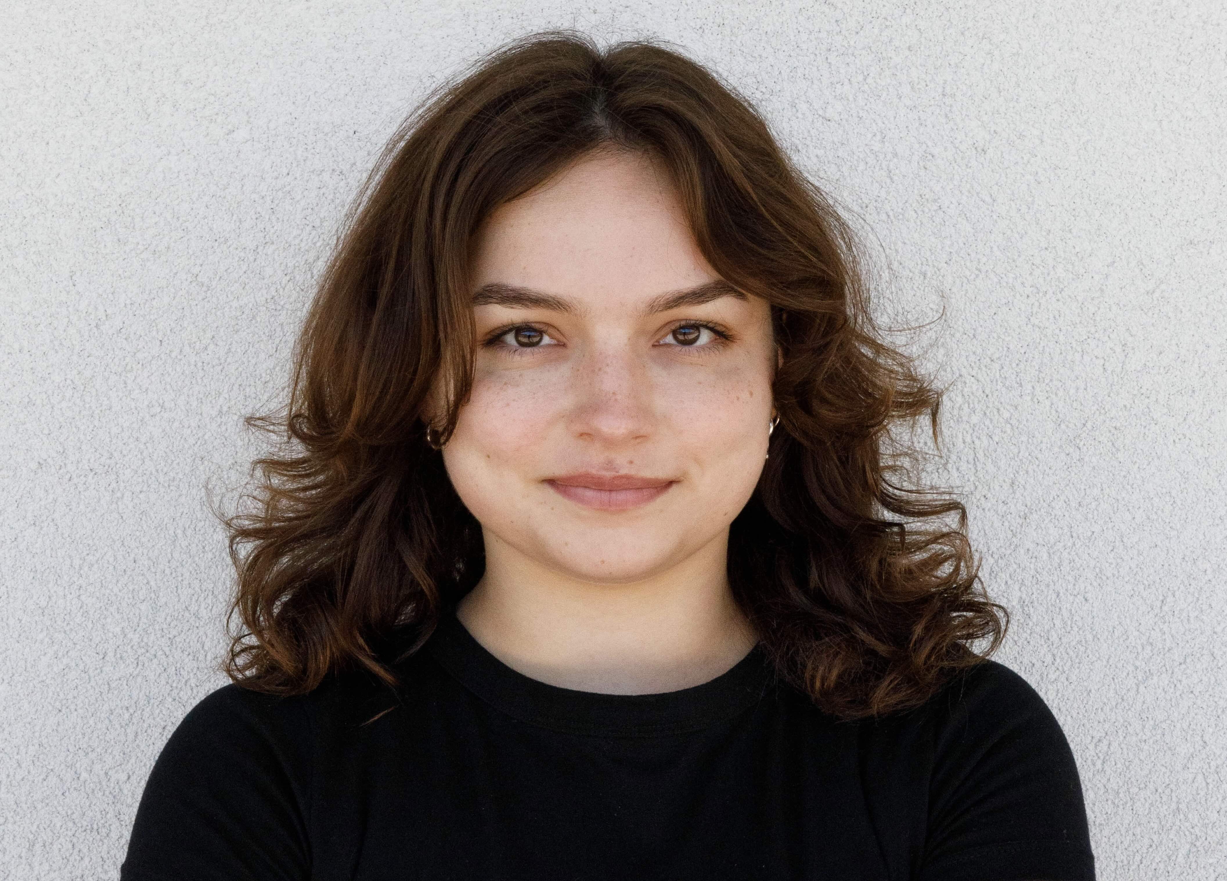 Close up headshot of student worker Dorothy Hamilton. She is pictured smiling, and wearing silver earrings and a black shirt. Her hair is curly and shoulder length.