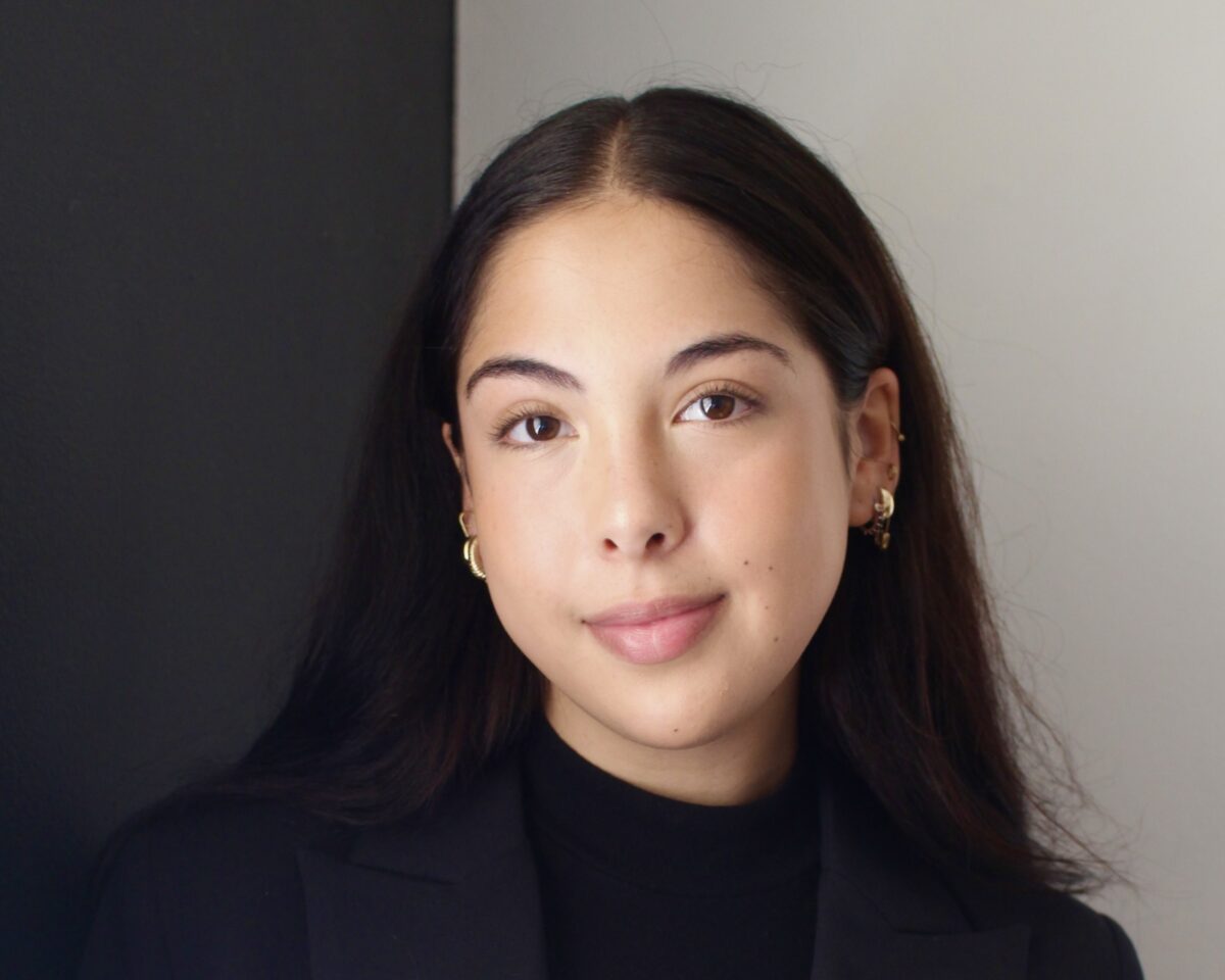 Headshot of UCSB Alum Eva Solis Lindholm. She is pictured in front of a dual tone neural background. She is wearing gold earrings and smiling.