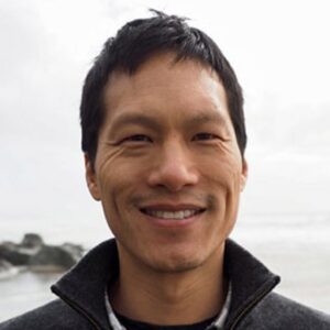 Close up head shot of moderator and professor Jia Ching Chen. He is pictured smiling and wearing a sweater in front of the ocean.
