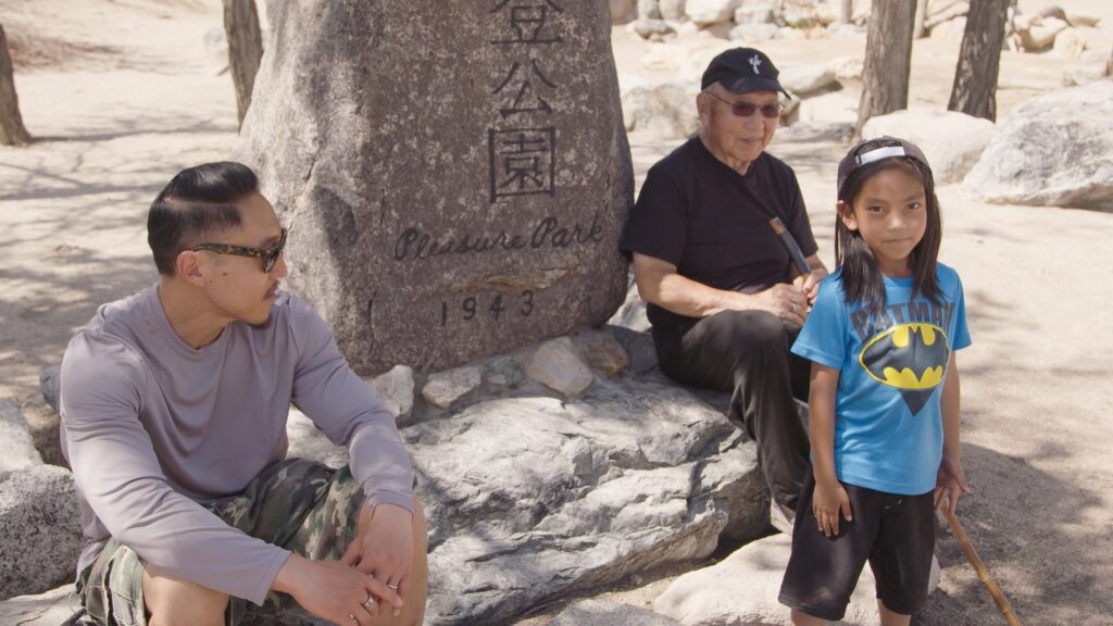 Three generations of the Nakamura family appear in this image flanking a sign reading 